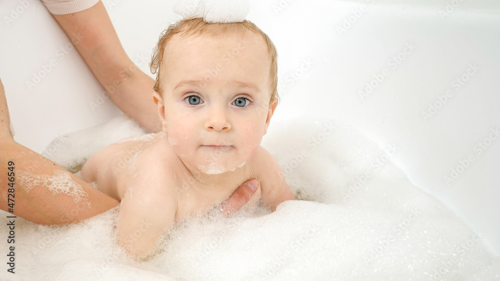 Funny baby boy with soap foam on head playing in bathroom with toy boats and ships. Concept of children hygiene, healthcare and development at home Funny baby boy with soap foam on head playing in bathroom with toy boats and ships. Concept of children hygiene, healthcare and development at home