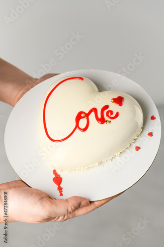 Mousse Heart shaped cake with the inscription love in the hands of a girl on gray background for Valentine's Day and February 14th