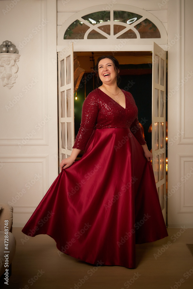 A beautiful majestic solemn fat queen in a red elegant dress in a beautiful hall in the palace. A chubby model poses during a photo shoot A beautiful majestic solemn fat queen in a red elegant dress in a beautiful hall in the palace. A chubby model poses during a photo shoot