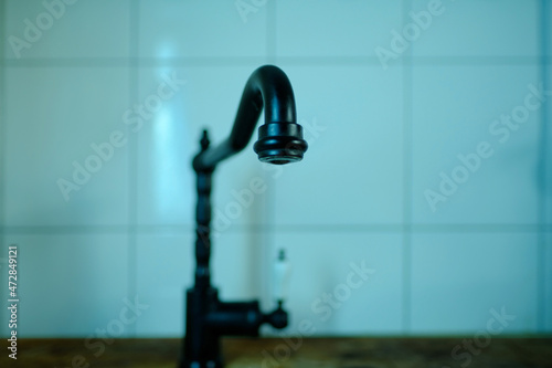 close-up of a black water faucet in a kitchen in a retro style, blurred background, green backlight, selective focus. concept of saving water resources, it is important to drink for human health photo