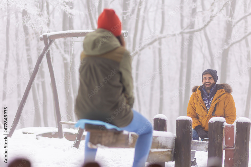 Couple sitting on seesaw having fun outdoor on snowy winter day Couple sitting on seesaw having fun outdoor on snowy winter day