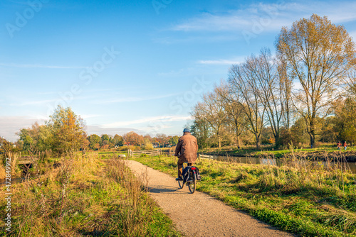 Unidentified man cycling on a cycle path along the water. The photo was taken in the Dutch nature reserve Markdal near the city of Breda, province of North Brabant, on a sunny but cold day in autumn.