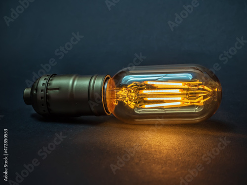 Glowing LED filament light bulb with an amber-colored glass shell on the dark background. Close-up