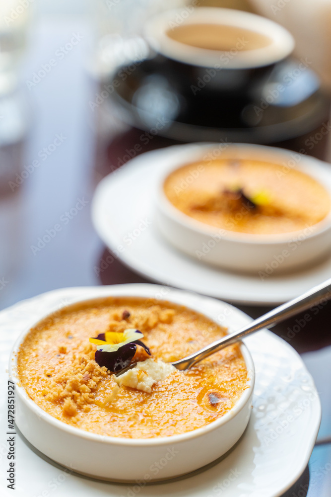 Spoon in creme brulee dessert served with coffee in cafe. Natural light, vertical, selective focus Spoon in creme brulee dessert served with coffee in cafe. Natural light, vertical, selective focus