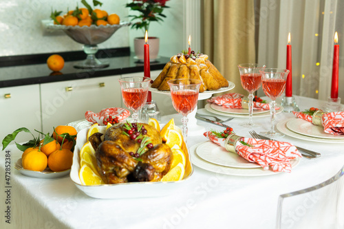 Beautifully decorated festive table with baked chicken, homemade cake, glasses of wine and candles. Baked chicken for Thanksgiving, Christmas and New Year.