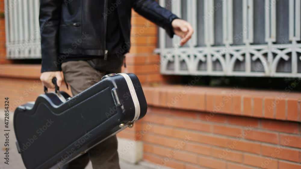 Man stroll down the street with a guitar case