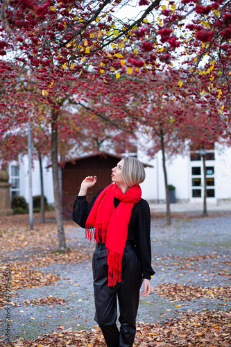 Walking european white young woman with blonde hair in red scarf in autumn