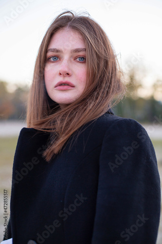 Portrait of cold long straight haired white european woman in dark coat in autumn on the beach