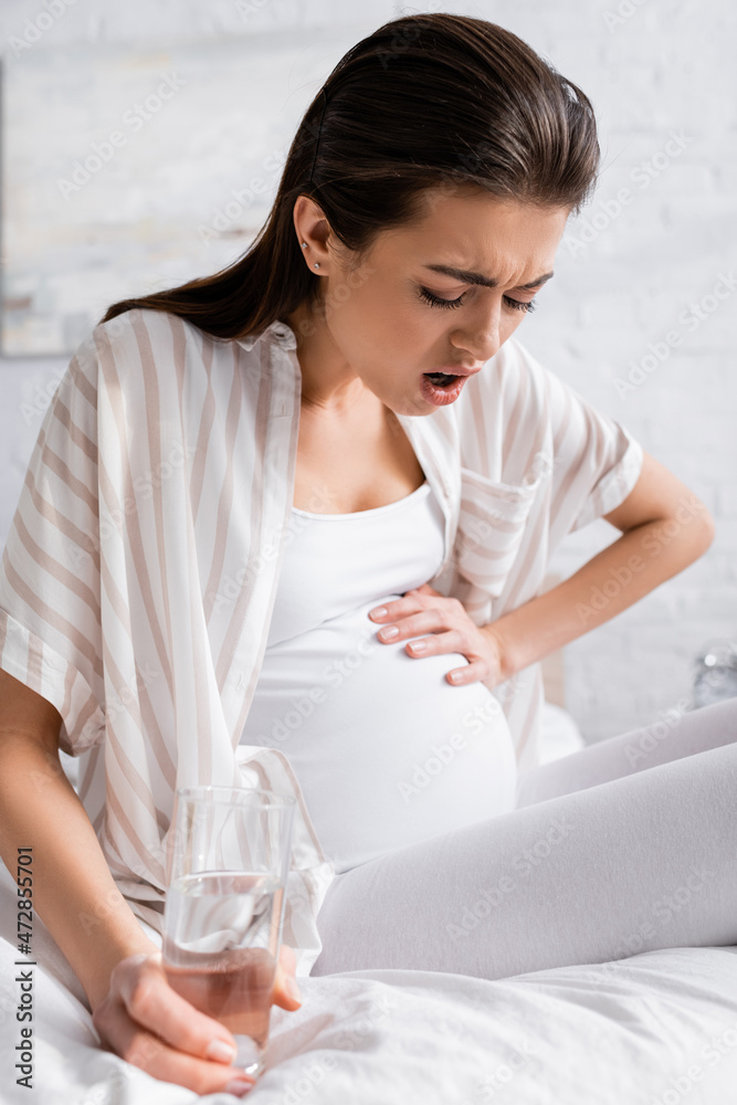 pregnant woman feeling cramp while holding glass of water. pregnant woman feeling cramp while holding glass of water.