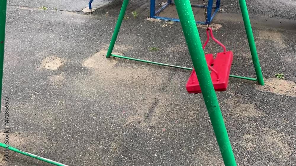 Empty red wooden swing swinging in the rain Empty red wooden swing swinging in the rain