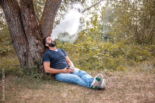 Stylish brutal vape man vaping an electronic cigarette out in the forest. Health concept.