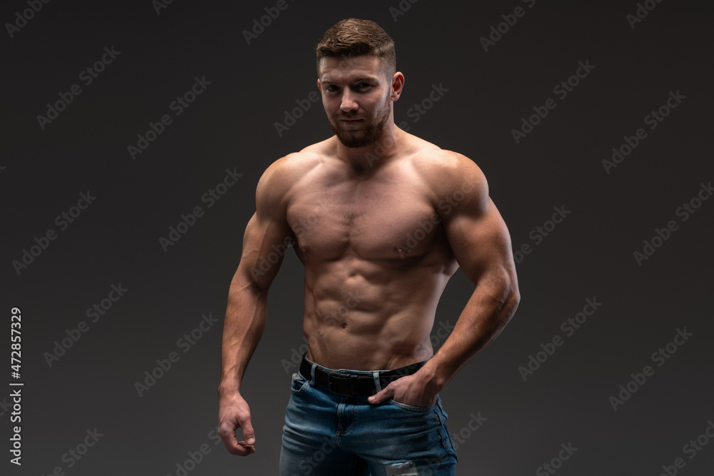 Waist up portrait view of the bodybuilder posing and showing his muscle definition. Man in good shape against dark background