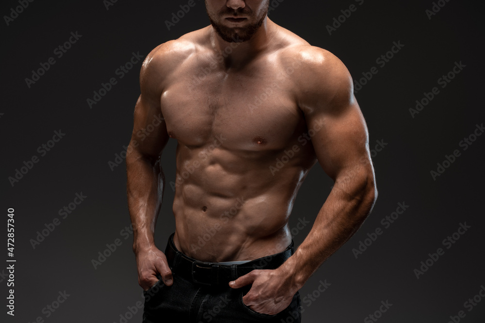 Close up of torso of healthy male athlete standing in trousers. He is showing his waist isolated on black background Close up of torso of healthy male athlete standing in trousers. He is showing his waist isolated on black background