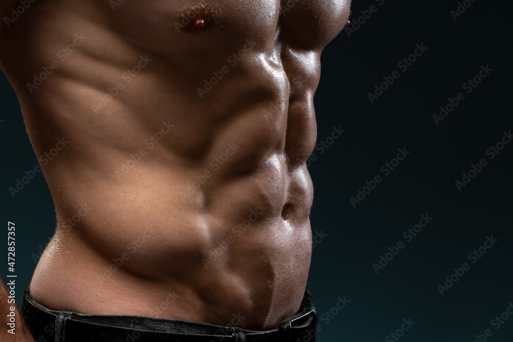 Fototapeta premium Strong athletic man fitness model posing isolated on black background. Cropped view of the male body with perfect abs