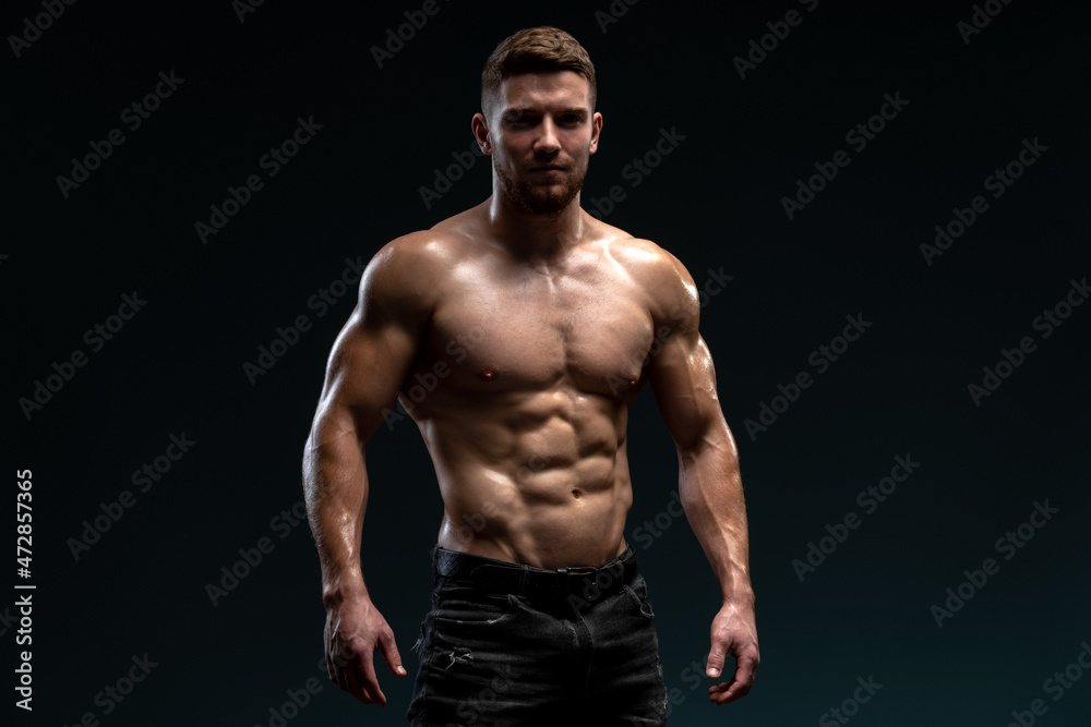Young handsome male athlete showing muscles isolated on a dark background. Sport and bodybuilding concept