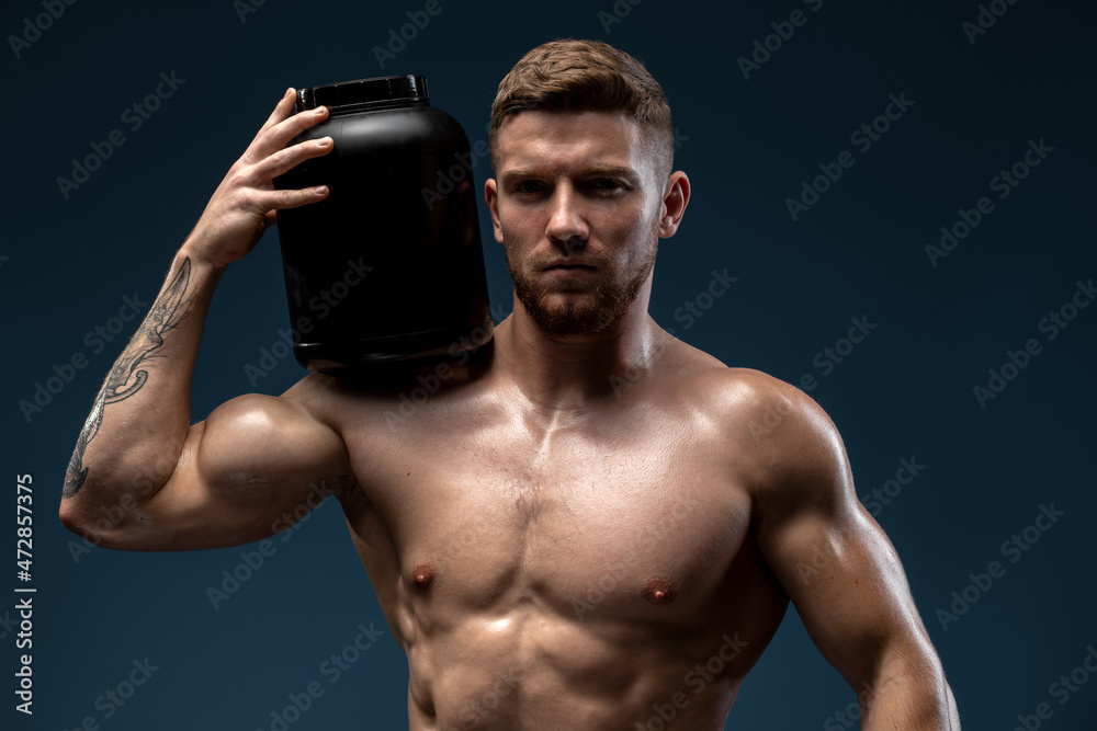 Waist up portrait of sporty handsome man with naked torso holding bottle with healthy protein drink, isolated over black studio background