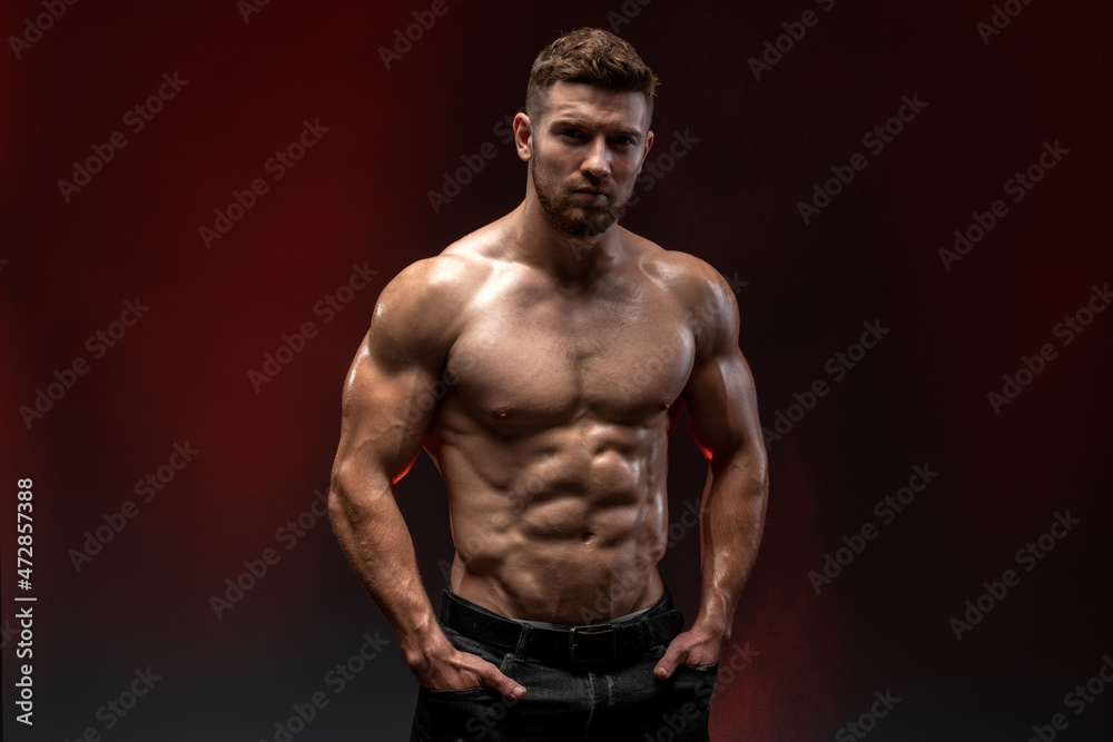 Fitness model showing his perfect body isolated on dark background. Bodybuilder man with perfect abs, shoulders, biceps, triceps and chest. Strong athletic man concept