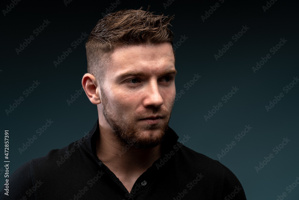 Portrait of the strong athletic man fitness model with perfect body wearing black t shirt looking away while posing isolated on dark background. Bodybuilding concept