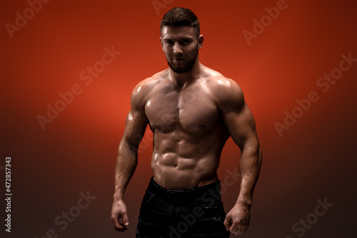 Serious sportsman is looking at the camera while standing at the studio. His torso is naked. Isolated on red background