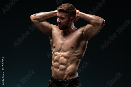 Serious sportsman is looking away while standing at the studio. His torso is naked. Isolated on black background