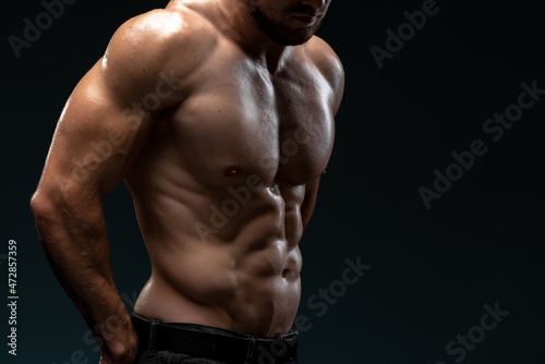 Cropped view of the male body with perfect abs posing isolated on black background. Strong athletic man fitness model