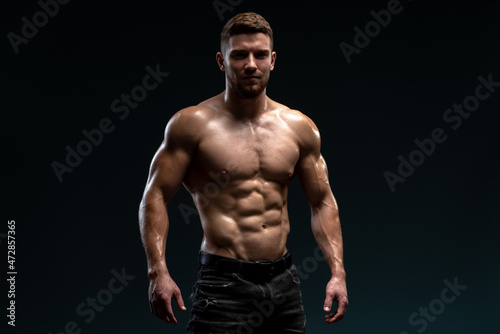 Young handsome male athlete showing muscles isolated on a dark background. Sport and bodybuilding concept