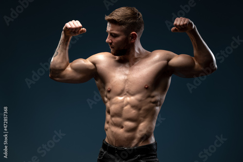 Young athletic man with a naked torso showing his biceps isolated on a dark blue background. Bodybuilding and strong people concept