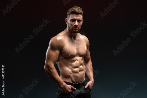 Horizontal view of the handsome muscular guy posing isolated on black background, while showing his strong body and muscles