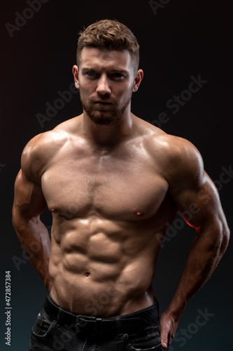 Vertical shot of the handsome muscular guy posing isolated on black background, while showing his strong body and muscles