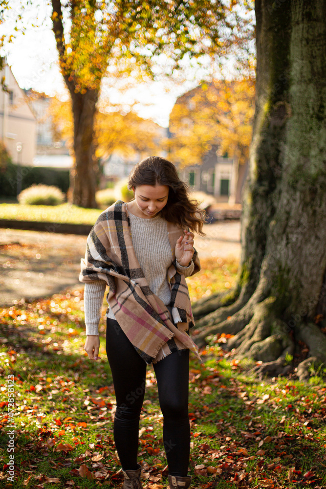 Walking young european white woman with brown hair with warm autumn scarf with trees behind Walking young european white woman with brown hair with warm autumn scarf with trees behind