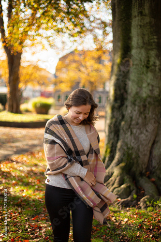 Walking european white young woman with brown hair with warm autumn scarf with trees behind