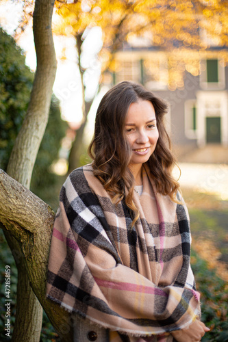 Pretty young woman with brown curly hair in warm scarf in autumn park
