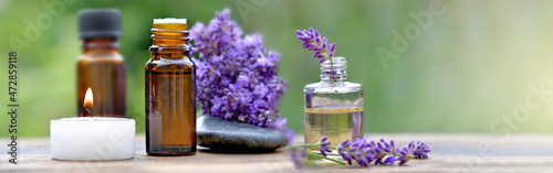 bottles of essential oil among lavender flowers arranged on a wooden table wi...