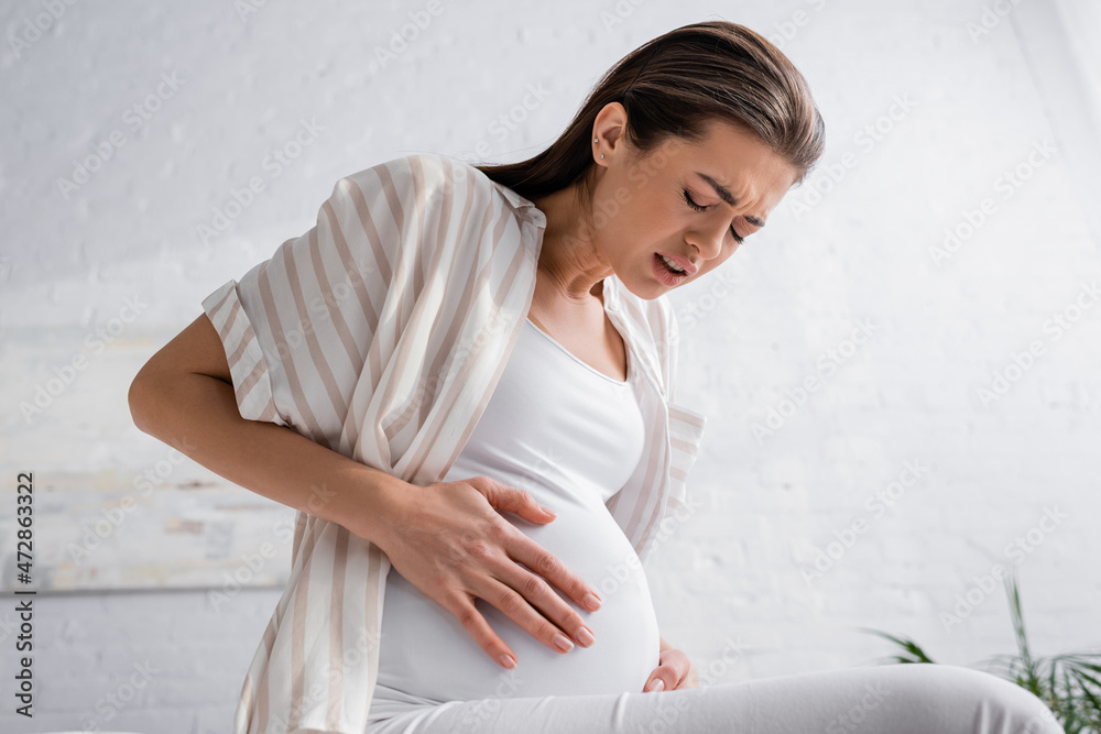 young pregnant woman with closed eyes feeling abdominal pain.