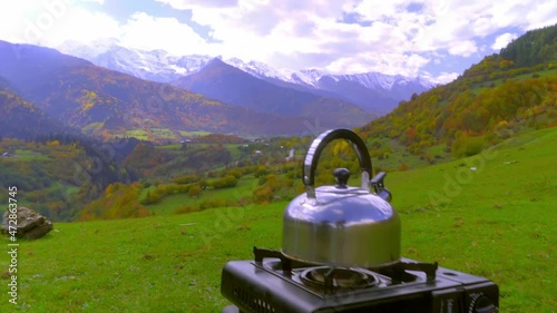 camping kettle is on portable camping gas stove, water is heated, camping. at top of the hill against the background of the mountain close-up. Svaneti Plain in Georgia. Making tea or coffee. Tourist. photo