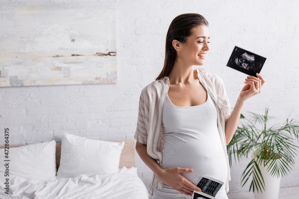 © LIGHTFIELD STUDIOS - smiling and pregnant woman holding ultrasound scans. © LIGHTFIELD STUDIOS - smiling and pregnant woman holding ultrasound scans.