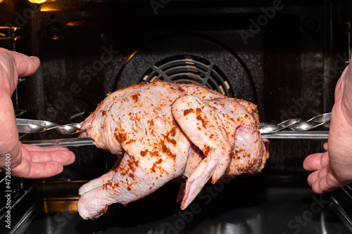 Hands putting raw whole chicken to roast in the oven, close-up. Preparing a meat dish for a festive dinner. Natural homemade healthy food
