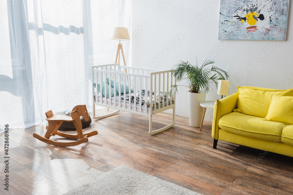 spacious room with yellow sofa, baby crib and rocking horse. - obrazy, fototapety, plakaty 