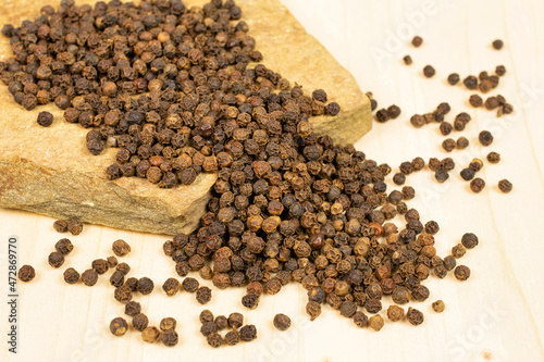 Lot of whole spicy black pepper with natural flat rock on plain wood