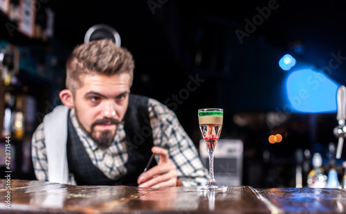 Charming bartender pouring fresh alcoholic drink into the glasses at the bar counter