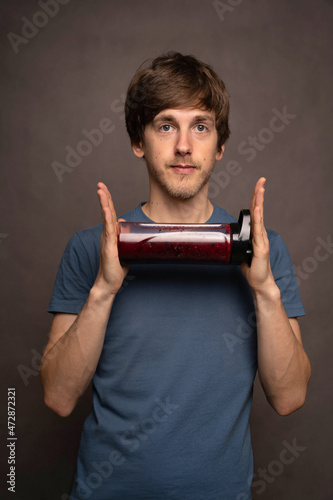 Young handsome tall slim white man with brown hair holding smoothie bottle horizontaly in grey shirt on grey background photo