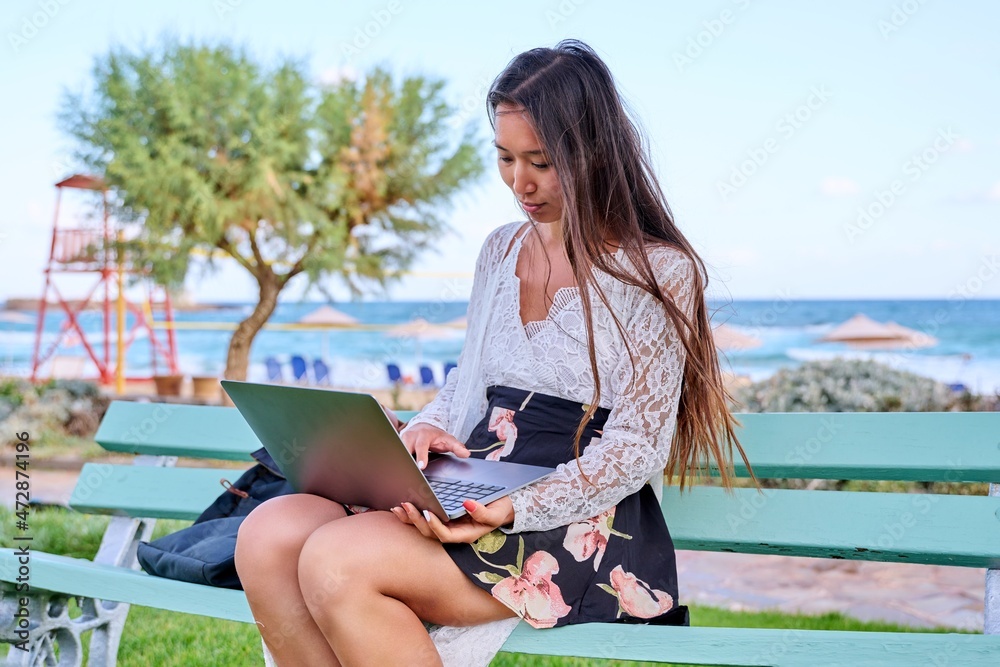 Beautiful young Asian woman using laptop sitting on an outdoor bench Beautiful young Asian woman using laptop sitting on an outdoor bench