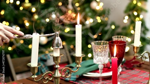 Close-up a female hand with a candle snuffer puts out candles on a festive table against the background of a Christmas tree photo