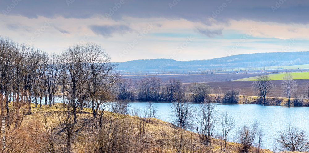 Fototapeta premium Spring landscape with river, trees by the river and plowed field on a sunny day