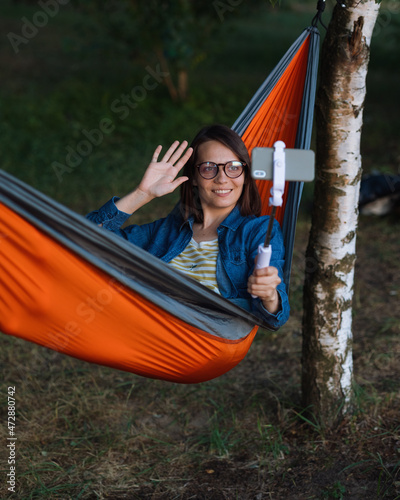 a European woman in a hammock in nature speaks via video link with a webcam. a female travel blogger creates video content. hiking and outdoor recreation on the seashore or in the forest. a cozy