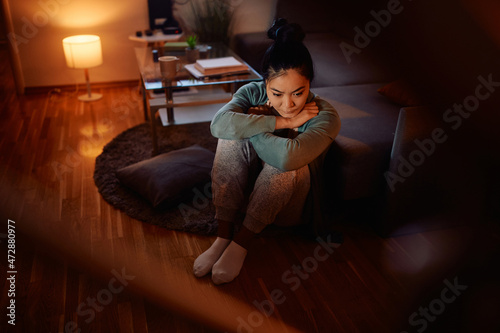 Depressed Asian woman feels lonely and thinks while sitting alone in dark at home.