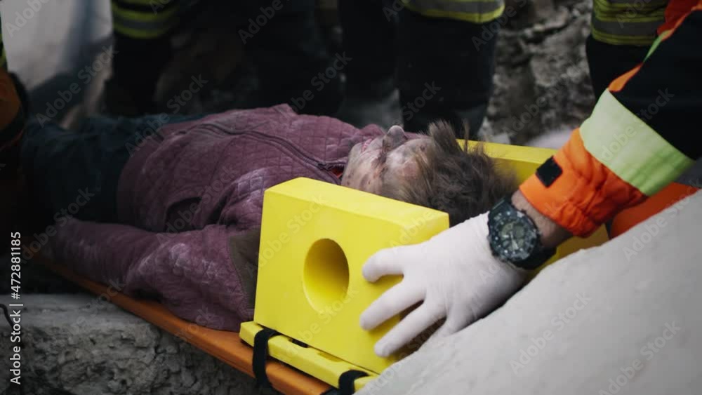 Tracking shot of crop emergency service workers lifting and carrying spinal board with injured teen survivor during rescue mission on remains of building destroyed by earthquake