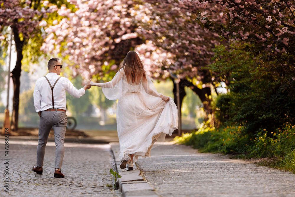Passion and love concept. Young man and woman walking together in blooming garden on spring day. Couple holding hands to each other near sakura trees. Couple in love spend time in spring garden.