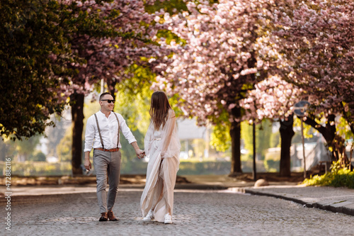 Passion and love concept. Young man and woman walking together in blooming garden on spring day. Couple holding hands to each other near sakura trees. Couple in love spend time in spring garden.