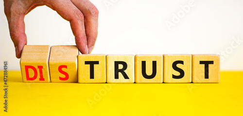 Distrust or trust symbol. Businessman turns wooden cubes, changes words 'distrust' to 'trust'. Beautiful yellow table, white background. Business and distrust or trust concept, copy space.